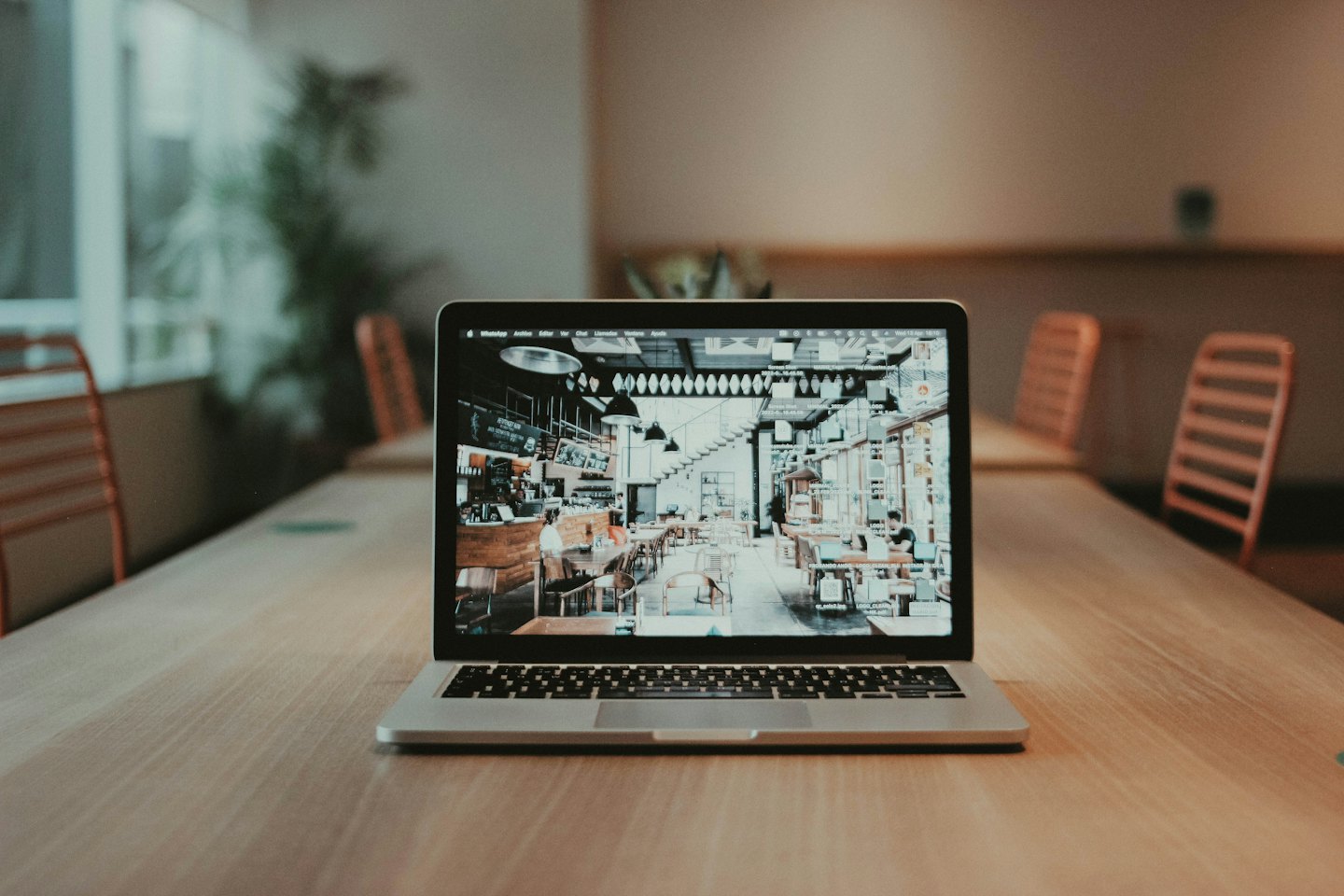 Laptop z widokiem wnętrza kawiarni na jasnym drewnianym stole.